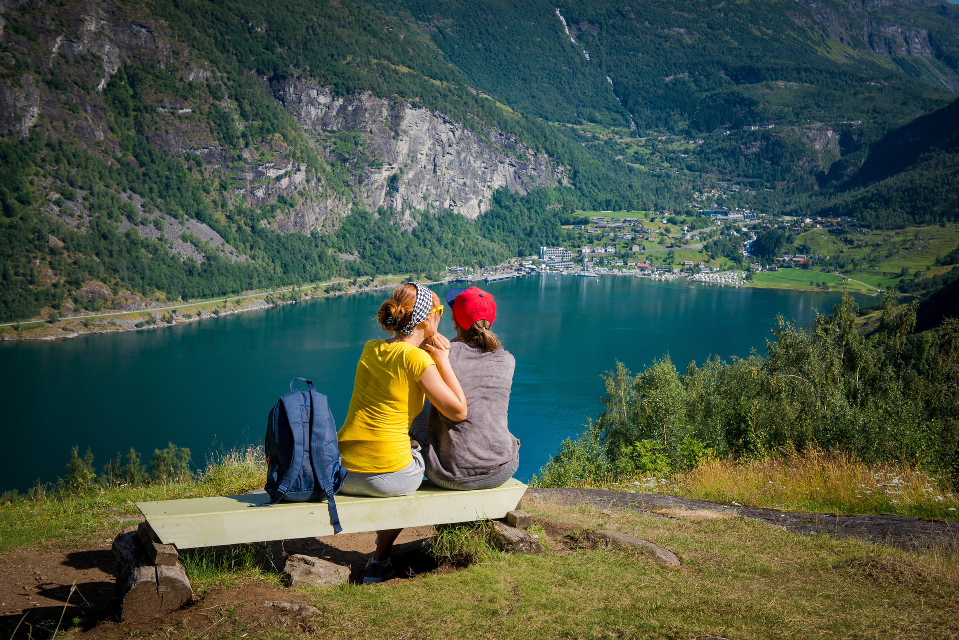 To personer som sitter på en trebenk og ser utover norsk fjord. Foto